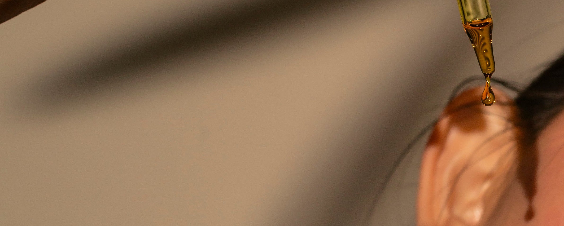 Dropper with liquid being applied to a person's skin on a neutral background